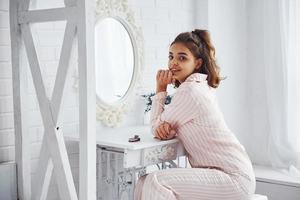 chica en ropa de dormir se sienta cerca del espejo en casa a la hora de la mañana foto