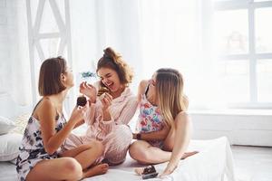 Eating sweets together. Happy female friends having good time at pajama party in the bedroom photo