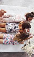 Top view of happy female friends that lying on the bed and having good time at pajama party in the bedroom photo