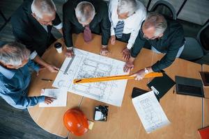 Top view of aged team of elderly businessman architects have a meeting in the office and works with plan photo