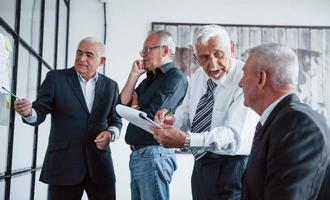 trabajando con pegatinas sobre vidrio. un equipo anciano de arquitectos de hombres de negocios mayores tiene una reunión en la oficina foto