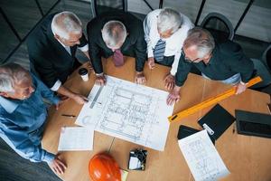 Top view of aged team of elderly businessman architects have a meeting in the office and works with plan photo
