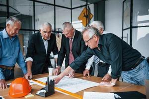 Planning construction by measuring it on paper. Aged team of elderly businessman architects have a meeting in the office photo