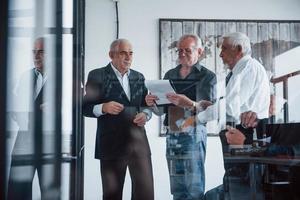 trabajando con pegatinas sobre vidrio. un equipo anciano de arquitectos de hombres de negocios mayores tiene una reunión en la oficina foto