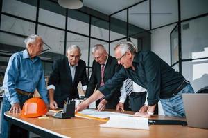 Planning construction by measuring it on paper. Aged team of elderly businessman architects have a meeting in the office photo