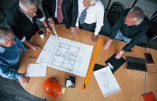 Top view of aged team of elderly businessman architects have a meeting in the office and works with plan photo