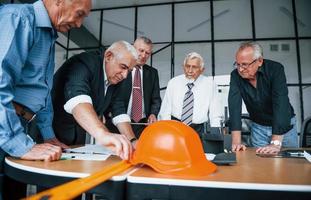 Planning construction by measuring it on paper. Aged team of elderly businessman architects have a meeting in the office photo