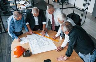 Aged team of elderly businessman architects works with plan in the office photo