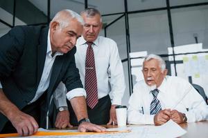 Planning construction by measuring it on paper. Aged team of elderly businessman architects have a meeting in the office photo