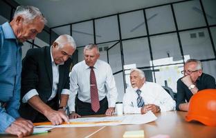 Planning construction by measuring it on paper. Aged team of elderly businessman architects have a meeting in the office photo