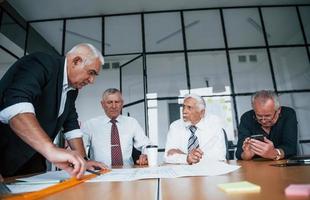 Planning construction by measuring it on paper. Aged team of elderly businessman architects have a meeting in the office photo