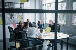 Stickers on the glass. Aged team of elderly businessman architects have a meeting in the office with young woman photo