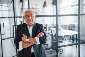Portrait of senior man that stands in front of aged team of elderly businessman architects that have a meeting in the office photo