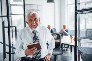 Portrait of senior man that stands in front of aged team of elderly businessman architects that have a meeting in the office photo