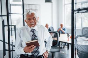 Portrait of senior man that stands in front of aged team of elderly businessman architects that have a meeting in the office photo