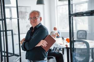 Portrait of senior man that stands in front of aged team of elderly businessman architects that have a meeting in the office photo