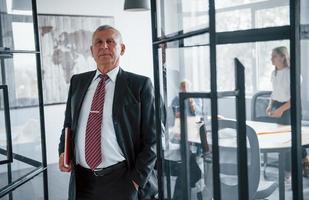 Portrait of senior man that stands in front of aged team of elderly businessman architects that have a meeting in the office photo