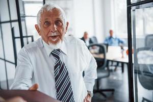 Portrait of senior man that stands in front of aged team of elderly businessman architects that have a meeting in the office photo