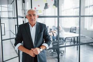 Portrait of senior man that stands in front of aged team of elderly businessman architects that have a meeting in the office photo