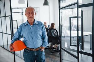 Portrait of senior man that stands in front of aged team of elderly businessman architects that have a meeting in the office photo