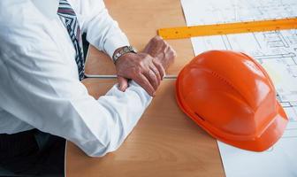 Close up view of senior businessman hands, hard hat and architect project on the table photo