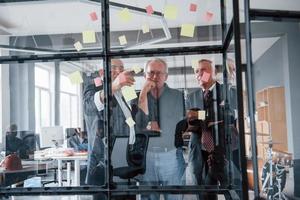 funciona con pegatinas en el cristal. un equipo anciano de arquitectos de hombres de negocios mayores tiene una reunión en la oficina foto