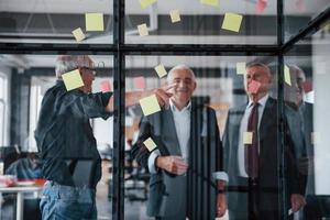 funciona con pegatinas en el cristal. un equipo anciano de arquitectos de hombres de negocios mayores tiene una reunión en la oficina foto