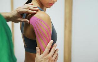 Doctor helps woman by shoulder treatment with kinesio tape photo