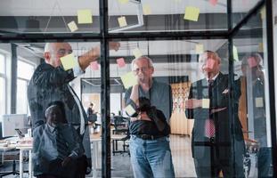 funciona con pegatinas en el cristal. un equipo anciano de arquitectos de hombres de negocios mayores tiene una reunión en la oficina foto