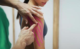 Doctor helps woman by shoulder treatment with kinesio tape photo