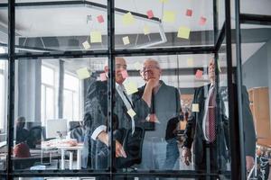 funciona con pegatinas en el cristal. un equipo anciano de arquitectos de hombres de negocios mayores tiene una reunión en la oficina foto