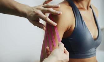 Doctor helps woman by shoulder treatment with kinesio tape photo