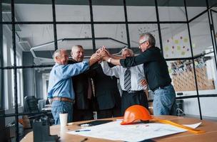 Job well done, gives high five to each other. Aged team of elderly businessman architects stands in the office together photo