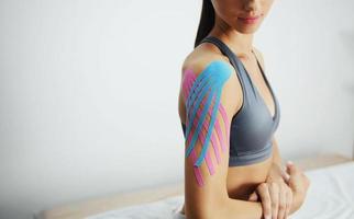 Sportive woman sits indoors with kinesio tape on her shoulder photo