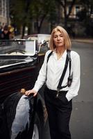 Blonde woman in black retro clothes near old vintage classic car photo