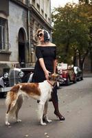 Blonde woman in sunglasses and in black dress near old vintage classic car with her dog photo