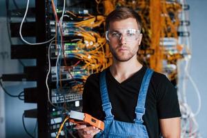 joven con gafas protectoras trabaja con equipos de internet y cables en la sala de servidores foto