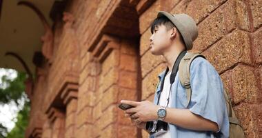 Seitenansicht eines glücklichen asiatischen Reisenden, der am Telefon tippt, während er am alten Tempel steht. junger Mann mit Handy. urlaubs-, technologie-, reise- und hobbykonzept. video