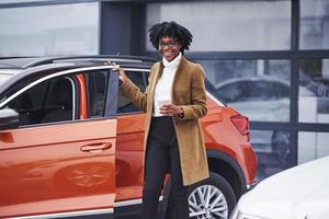 Young african american woman in glasses stands outdoors near modern car photo