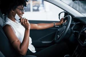 Having a call. Young african american woman sits inside of new modern car photo