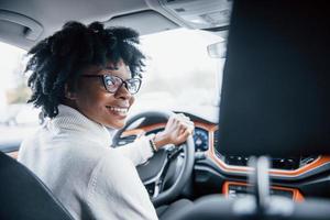 Looks back. Young african american woman sits inside of new modern car photo