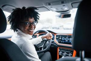 Looks back. Young african american woman sits inside of new modern car photo