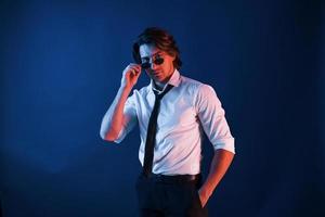 Beautiful man in formal wear and in glasses is in the studio with blue neon lighting photo