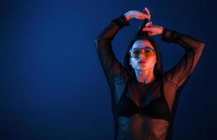 Hot brunette in sunglasses posing in the studio with neon lighting photo