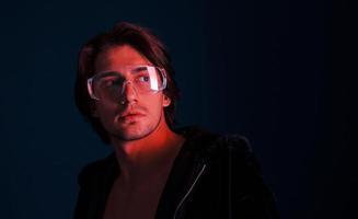 Beautiful long haired hot man in glasses is in the studio with blue neon lighting photo