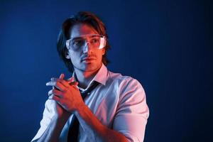 hermoso hombre con gafas y traje y corbata está en el estudio con luces de neón azul foto