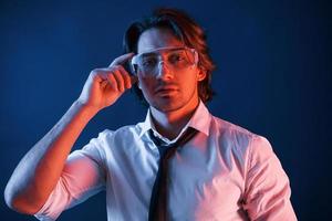 hermoso hombre con gafas y traje y corbata está en el estudio con luces de neón azul