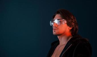 Beautiful long haired hot man in glasses is in the studio with blue neon lighting photo