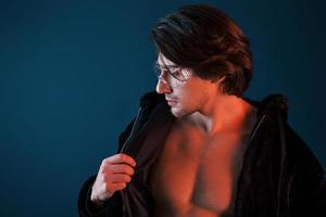 hermoso hombre caliente de pelo largo con gafas está en el estudio con luces de neón azul foto