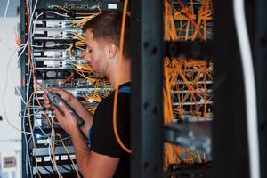 Young man in uniform works with internet equipment and wires in server room photo